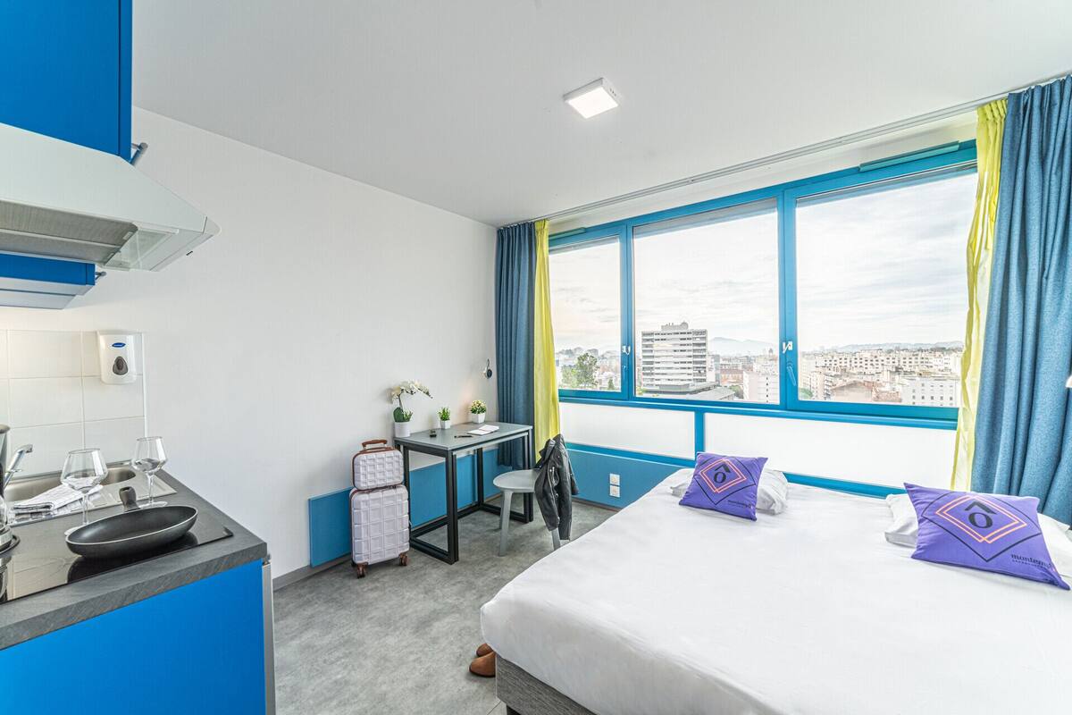 Habitación de hotel con cama, escritorio, ventana con vista a la ciudad, kitchenette y baño.