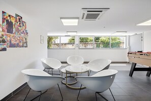 Een moderne kamer met een tafelvoetbaltafel, een groot raam met uitzicht op groen, en een muur met kleurrijke kunstwerken.