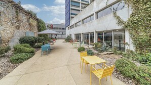 Un patio al aire libre con mesas y sillas, un muro de piedra y un edificio con amplias ventanas y un letrero.