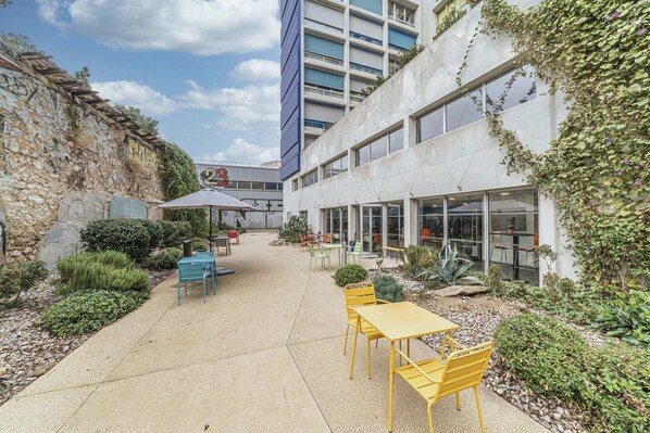 Un patio al aire libre con mesas y sillas, un muro de piedra y un edificio con amplias ventanas y un letrero.