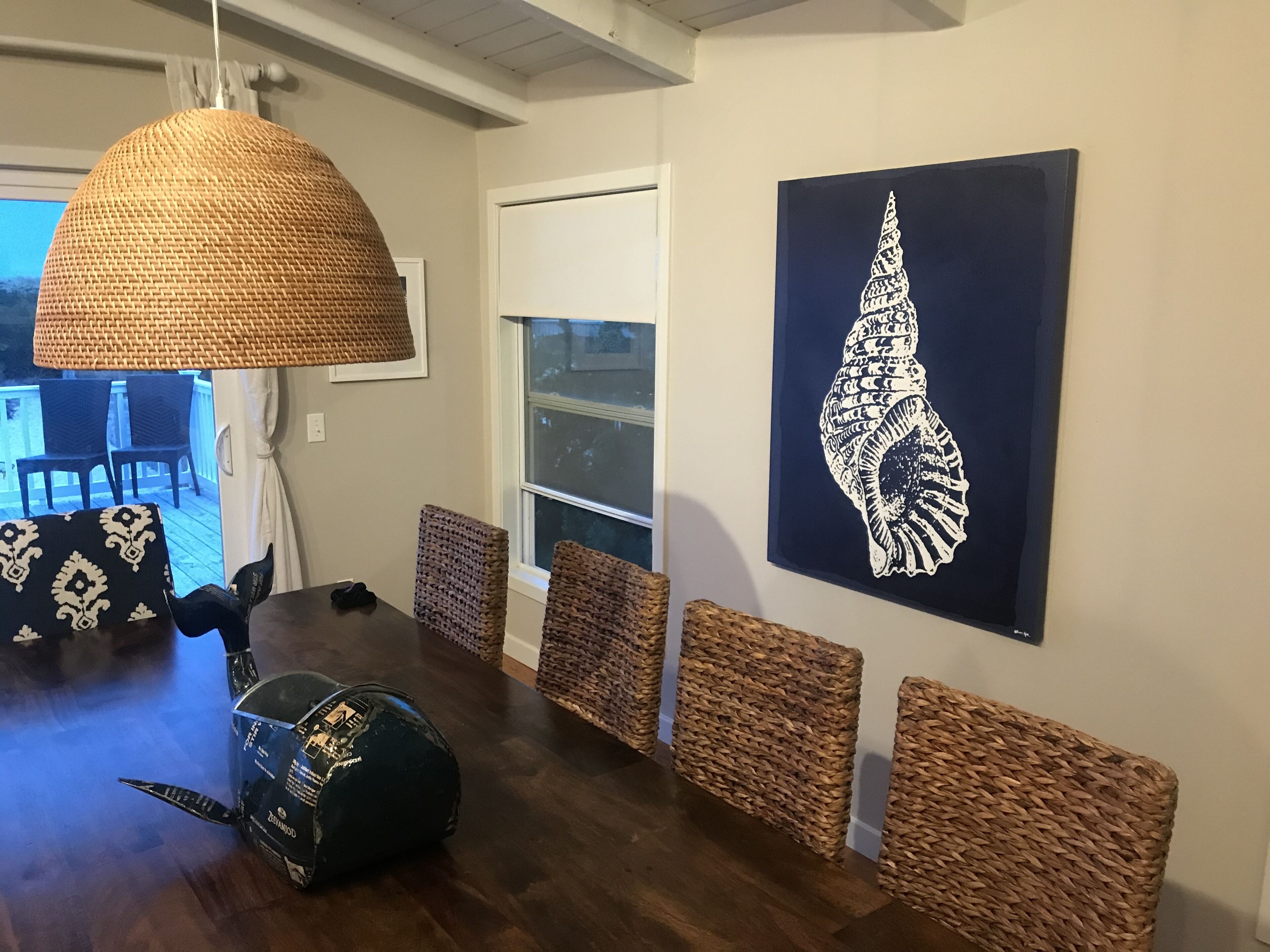 Un comedor con una mesa de madera oscura, sillas tejidas y una lámpara colgante grande de fibras.