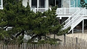 Een twee verdiepingen tellend strandhuis met een balkon en een trap naar de bovenverdieping.