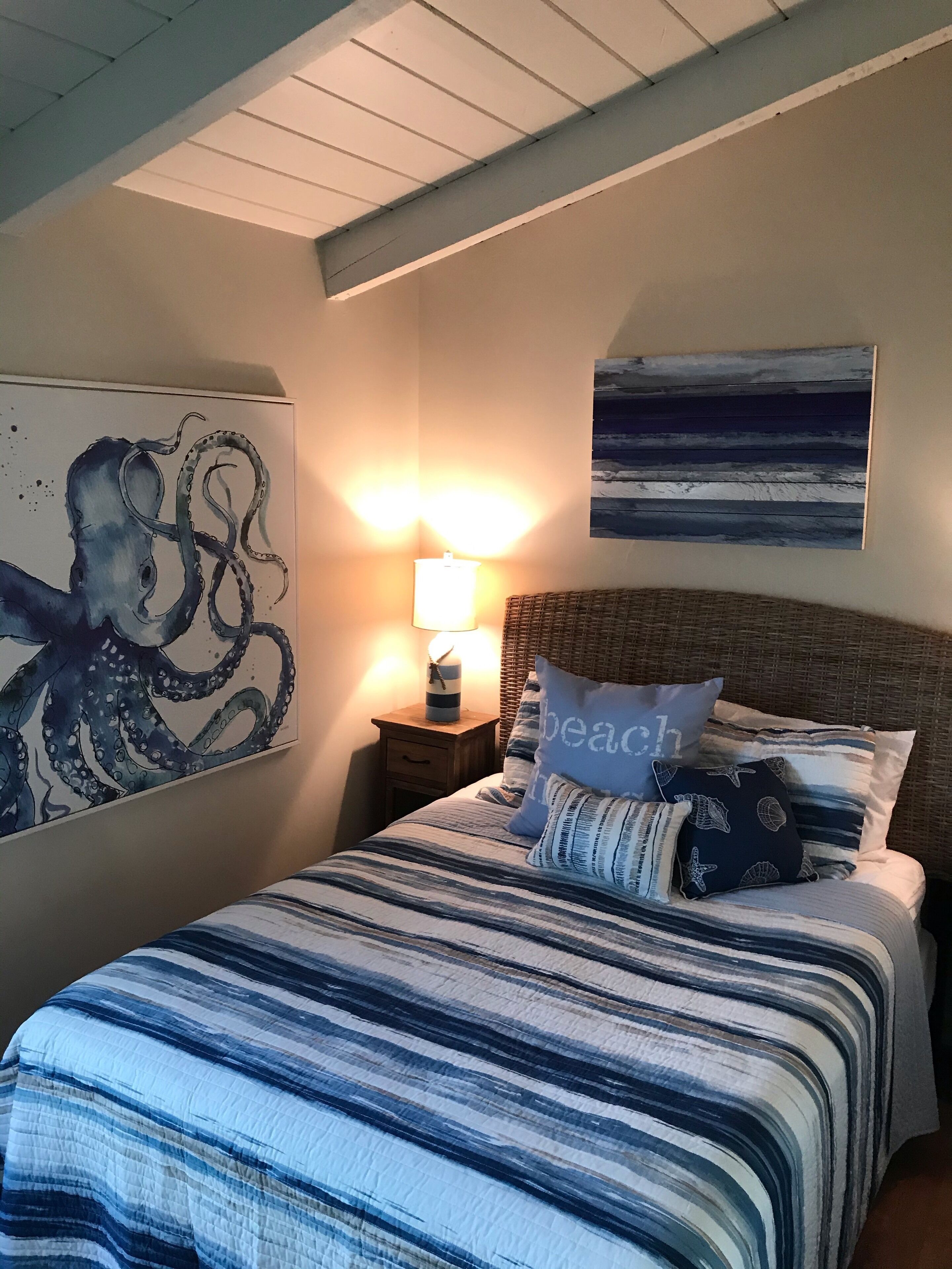 Un dormitorio con una cama, una mesita de noche, una lámpara, un cuadro y una obra de arte en la pared.
