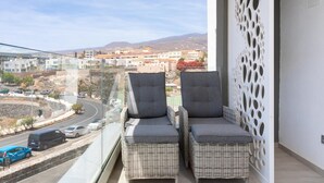 Un balcon avec des fauteuils en osier et une vue sur une ville côtière.