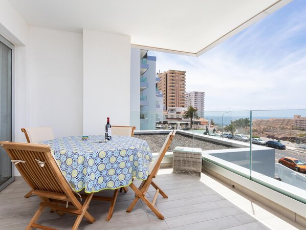 Un balcon avec une table et des chaises, une bouteille de vin et une vue sur le paysage urbain et la mer.
