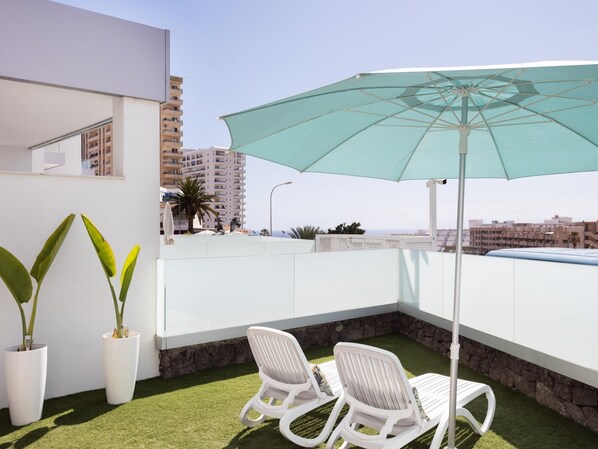 Een balkon met twee witte loungestoelen, een turquoise parasol en uitzicht op de stad.