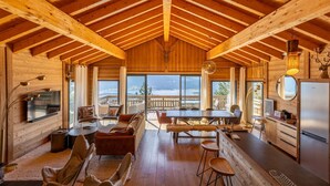 A spacious wooden cabin with a high ceiling, a dining area, a kitchen, and large windows offering a view of the outdoors. - Chalet with spa/heated pool, lake view, ski-in/ski-out access, fire pit, 5-star rating (Les Angles)
