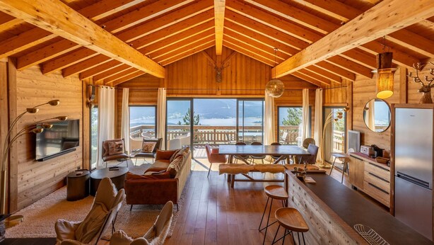 A spacious wooden cabin with a high ceiling, a dining area, a kitchen, and large windows offering a view of the outdoors. - Chalet with spa/heated pool, lake view, ski-in/ski-out access, fire pit, 5-star rating (Les Angles)