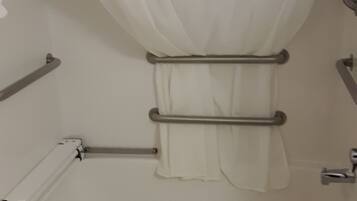 A bathroom with a bathtub, grab bars, and a shower curtain.