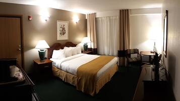 A hotel room with a large bed, two bedside tables with lamps, a desk with a chair, a TV, and a window with curtains.
