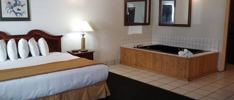 A hotel room with a large bed, a wooden bathtub, two wall-mounted mirrors, and a painting on the wall.