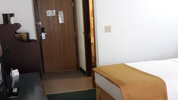 A hotel room with a bed, a desk, a chair, and a door.