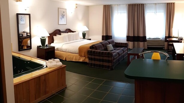 Habitación de hotel con cama, sofá, una mesita, espejo y una kitchenette con fregadero y estufa.