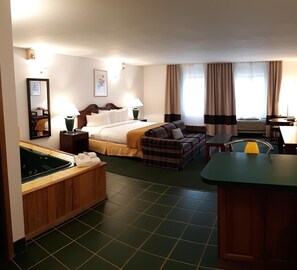 Une chambre d’hôtel comprenant un lit, un canapé, une petite table, un miroir et un coin cuisine équipé d’un évier et d’une cuisinière.