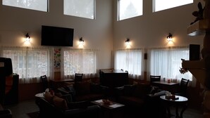 Un salón amplio con un televisor grande, varias zonas de estar y ventanas grandes con cortinas.