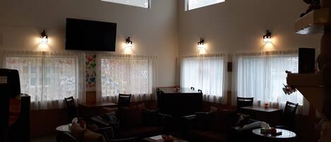 Un salón amplio con un televisor grande, varias zonas de estar y ventanas grandes con cortinas.