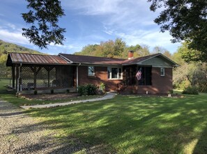 A single-story brick house with a covered porch, a front yard, and an American flag. - Isolate Stay at Pilot Mountain (Pinnacle)