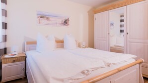 Una cama bien hecha con sábanas y almohadas blancas, una mesita de noche con una lámpara y un cuadro en la pared.