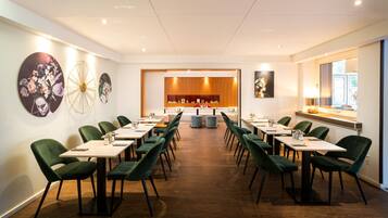 A conference room with a long table, green chairs, and a wooden panel wall.