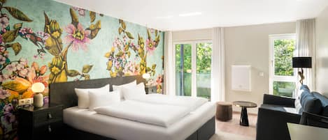 Habitación de hotel moderna con una cama grande, un escritorio, una silla y vistas a zonas verdes a través de las ventanas.
