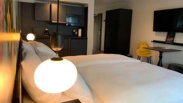 A hotel room with a bed, a desk, a chair, a television, and a kitchenette.