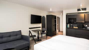 Une chambre d’hôtel moderne équipée d’un canapé, d’une table à manger, d’une télévision, d’une armoire et d’une kitchenette.