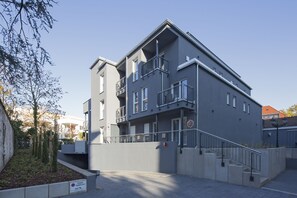 Un immeuble à plusieurs étages, doté d’une façade grise, de balcons et d’un escalier menant à l’entrée.