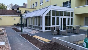 Een oranjerie met glazen dak, omringd door buiten zitplaatsen en een tuin.