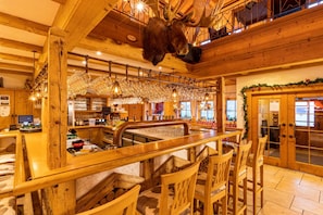 A rustic interior with wooden beams, a mounted moose head, bar area with stools, and a glass display. - Steig-Alm Hotel (Bad Marienberg)