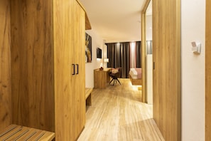 A hallway with wooden flooring, a bench, a desk with a chair, and a bed with a red and white checkered blanket. - Steig-Alm Hotel (Bad Marienberg)