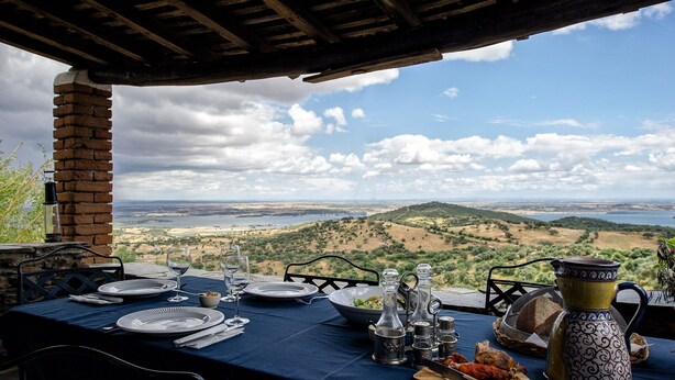 Mesa posta para refeição com vista panorâmica para colinas e um corpo d'água.