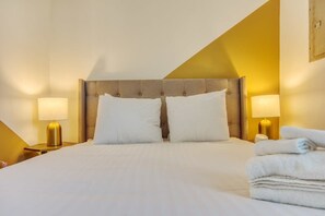 A hotel room with a large bed, two bedside lamps, and a stack of towels.