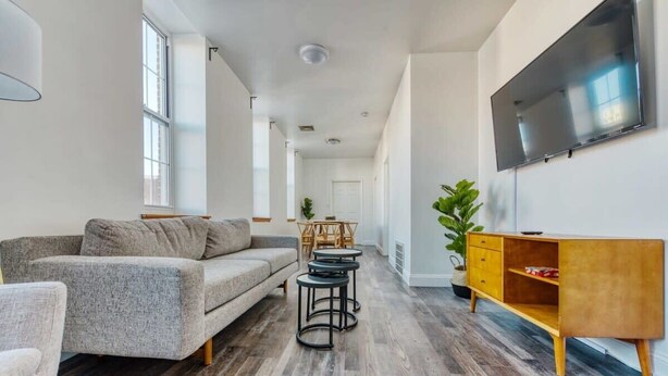 Una sala moderna con un sofá gris, una mesa de centro de madera y un televisor montado en la pared.