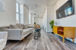 A modern living room with a grey sofa, a wooden coffee table, and a TV mounted on the wall.