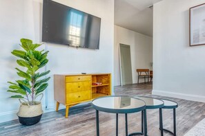 A modern living room with a flat-screen TV, a yellow cabinet, a potted plant, and three glass-top tables.