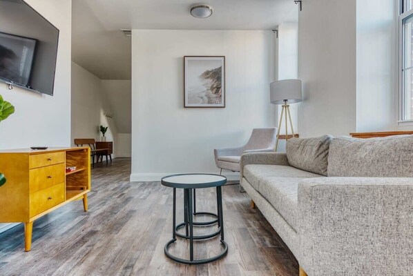 A modern living room with a sofa, a round coffee table, a TV mounted on the wall, and a framed picture on the wall.
