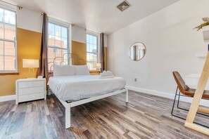 A modern bedroom with a white bed, a bedside table, a lamp, and a chair. - Stairway | 3BR Apt w W/D Ideal for Groups (Philadelphia)
