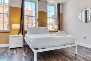 A modern bedroom with a white bed, two bedside tables, a round mirror, and large windows with curtains. - Stairway | 3BR Apt w W/D Ideal for Groups (Philadelphia)