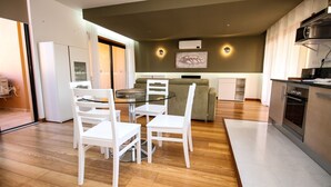 A modern kitchen with white cabinetry, a built-in oven, and a dining area with a glass table and white chairs. - LUXURY APARTMENT - T1 pool view - PRAIA DA LUZ (Luz)