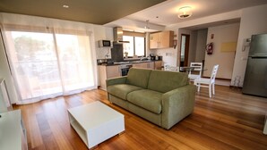 A compact living space with a kitchenette, a green sofa, a white coffee table, and a dining area with white chairs. - LUXURY APARTMENT - T1 pool view - PRAIA DA LUZ (Luz)