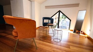 A modern room with a wooden floor, a large window, a blue chair, and an orange chair. - LUXURY APARTMENT - T1 pool view - PRAIA DA LUZ (Luz)