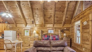 L’intérieur d’une cabane avec des murs en bois, un canapé en cuir, une table à manger avec des chaises et un coin cuisine.