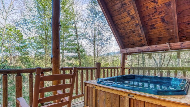 Une terrasse en bois avec un jacuzzi, une rambarde en bois et une chaise.