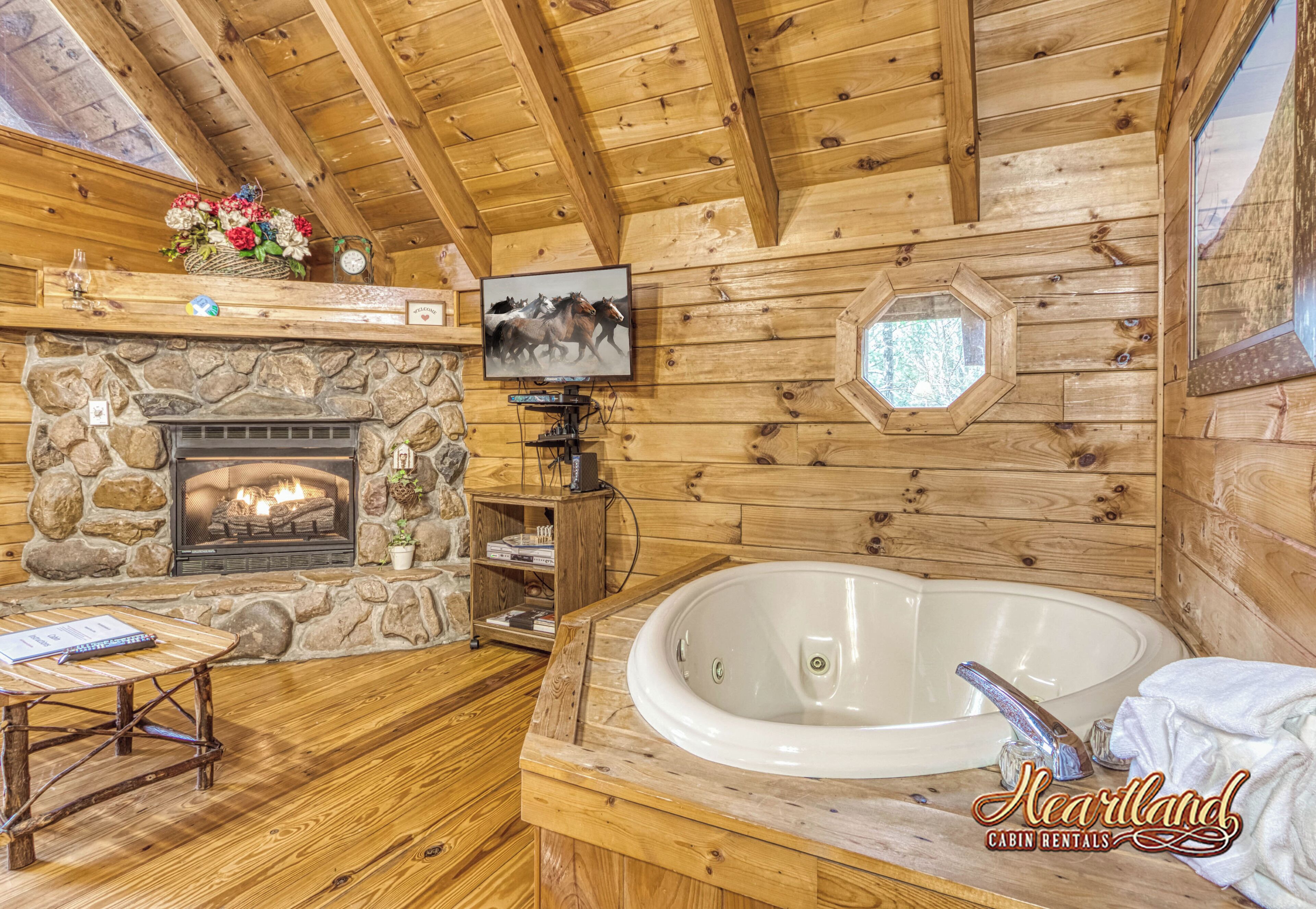 A cabin interior with a stone fireplace, a large bathtub, wooden walls, and a mounted television.