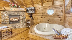 L’intérieur d’une cabane est agrémenté d’une cheminée en pierre, d’une grande baignoire, de murs en bois et d’un téléviseur fixé au mur.
