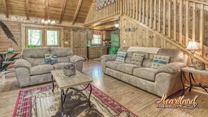 A cabin interior with two sofas, a dining table, a staircase, and wooden walls. - Located in a peaceful setting, convenient to both Gatlinburg and Pigeon Forge! (Sevierville)