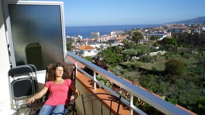 Un balcón con vistas a un pueblo costero, una silla y una ventana con mosquitera.