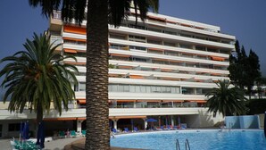 Un hotel de varios pisos con piscina, palmeras y mobiliario exterior.
