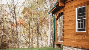 A wooden cabin with a stone foundation, surrounded by a forest with autumn-colored trees. - Old World Craftmanship with Modern Amenities (Bristol)