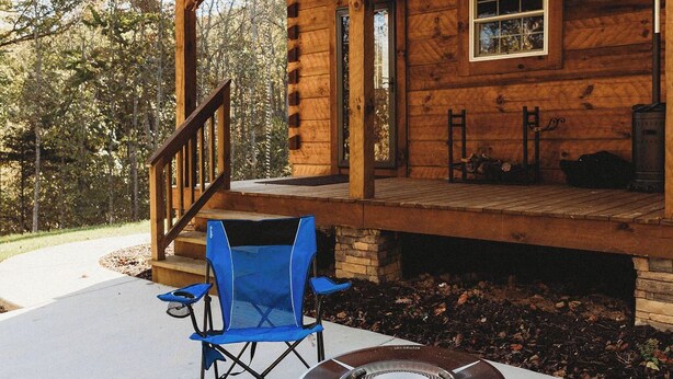 A wooden cabin with a covered porch, a fire pit, and blue folding chairs. - Old World Craftmanship with Modern Amenities (Bristol)